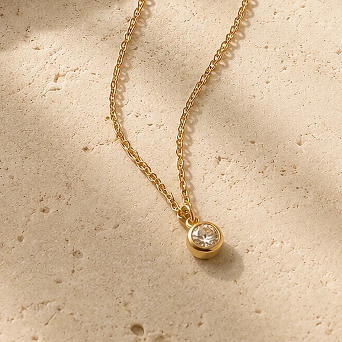 Close detail of a fine gold chain and a bezel-set stone in low sunlight