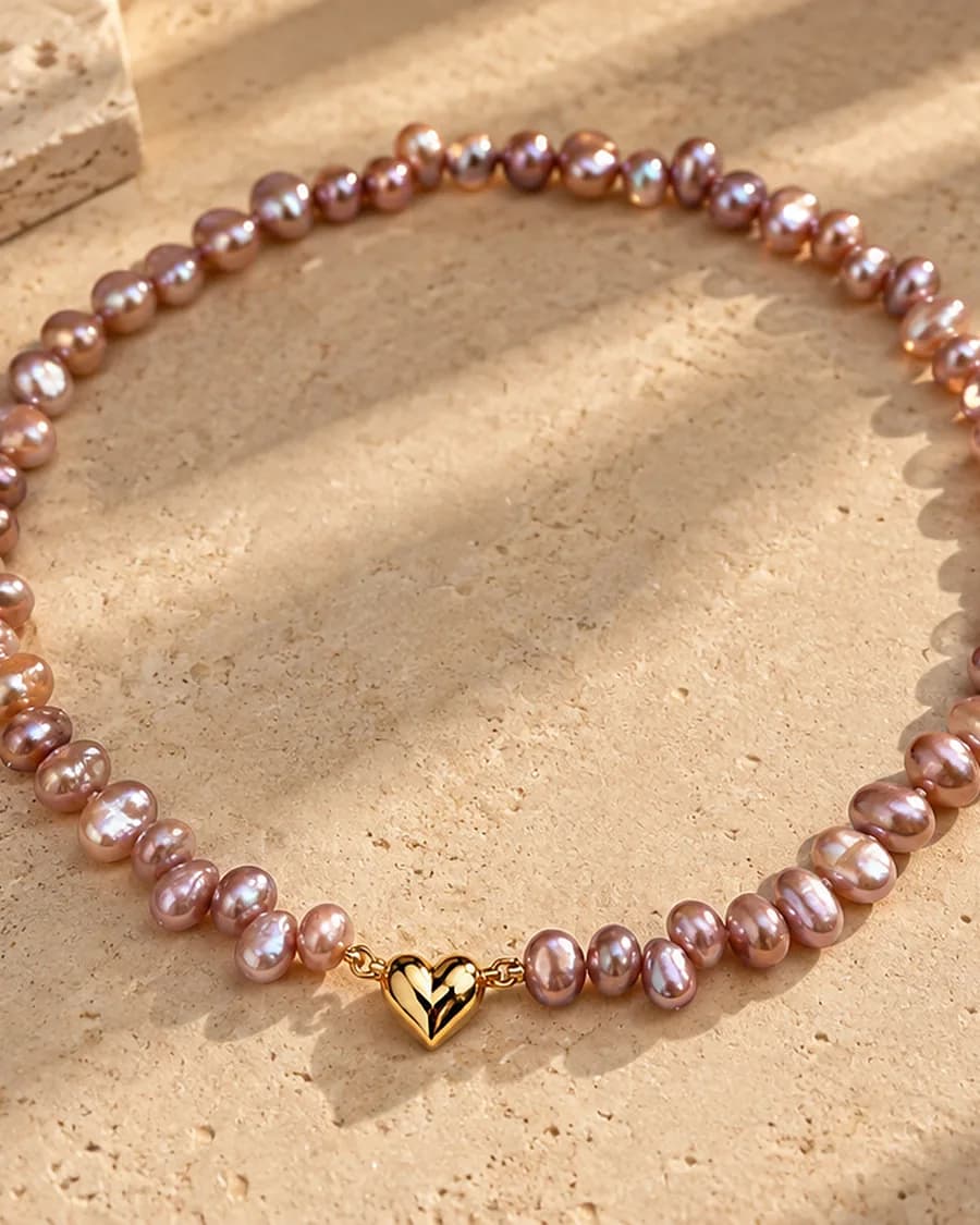 The Freshwater Pearl Rosé Amour Necklace photographed on a travertine block in warm daylight