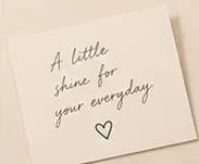 A cream SÉVRA card handwritten with “A little shine for your everyday”