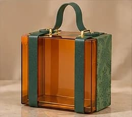 An amber acrylic SÉVRA suitcase gift box with green leather straps